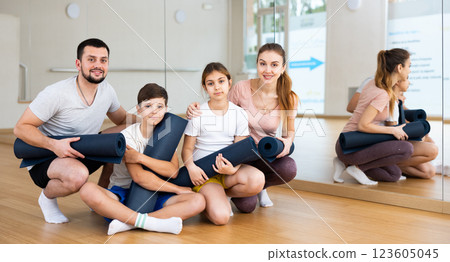 Smiling fit woman and man with teen children posing with yoga mats in gym 123605045