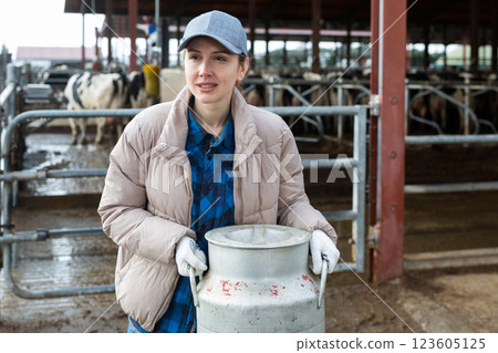 Milkmaid with aluminium cans near open cowshed at dairy farm 123605125