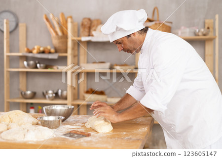 Caucasian guy works in bakery as baker, kneads dough, works with flour. 123605147