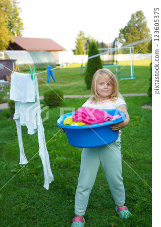 Standing with a plastic basin, the girl looks up at the drying clothes, her hair tousled by the breeze. Standing with a plastic basin, the girl looks up at the drying clothes, her hair tousled by the breeze. 123605375