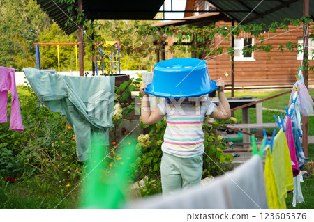 A young girl waits near the outdoor laundry line, gripping a plastic tub as the wind rustles the fabric. A young girl waits near the outdoor laundry line, gripping a plastic tub as the wind rustles the fabric. 123605376