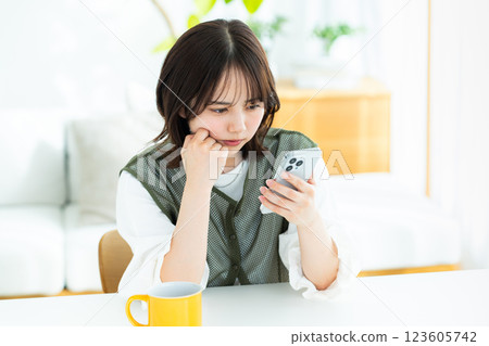 在房間裡操作智慧型手機的年輕女子 在房間裡操作智慧型手機的年輕女子 123605742