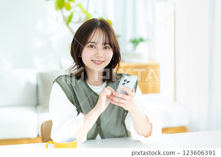 在房間裡操作智慧型手機的年輕女子 在房間裡操作智慧型手機的年輕女子 123606391