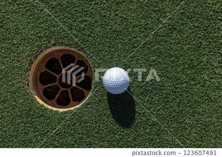 In the hole, White golf ball on green grass with golf hole, Golf ball ready to be shot, Golf ball close up on green grass in the hole, Top view. In the hole, White golf ball on green grass with golf hole, Golf ball ready to be shot, Golf ball close up on green grass in the hole, Top view. 123607491