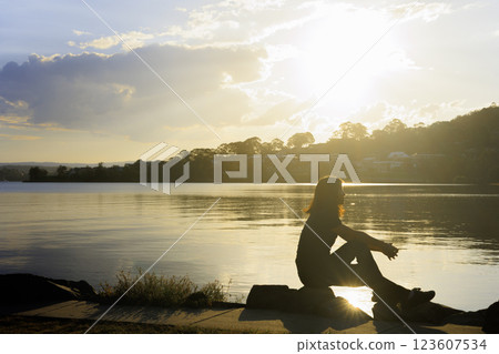 Profile of a woman sitting on a rock and watching the sunset 123607534