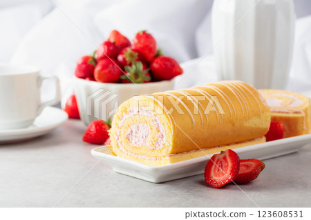 Delicious biscuit roll cake with fresh strawberries on a white stone table. 123608531