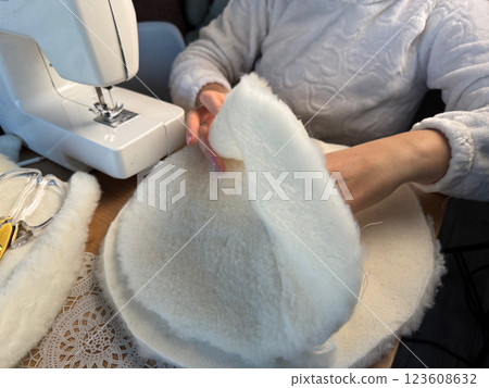 A woman is working at a sewing machine. She is sewing a pet bed from fur fabric. She is sewing the bottom of the bed. Oblique Angle. A woman is working at a sewing machine. She is sewing a pet bed from fur fabric. She is sewing the bottom of the bed. Oblique Angle. 123608632