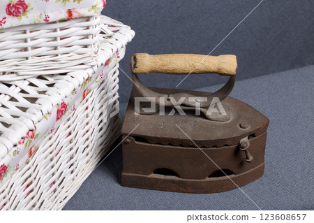 Old iron, heated by hot coals. Located on gray fabric. Nearby are wicker baskets. Old iron, heated by hot coals. Located on gray fabric. Nearby are wicker baskets. 123608657