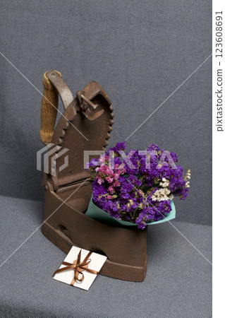 Old iron, heated by hot coals. A bouquet of dried flowers is embedded in the slightly open iron. Nearby is a greeting card. 123608691