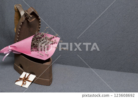 Old iron, heated by hot coals. A bouquet of dried flowers is embedded in the slightly open iron. Nearby is a greeting card. 123608692