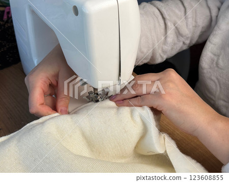 A woman is working at a sewing machine. She is sewing a pet bed from fur fabric. Close-up. Oblique Angle. Close-up. 123608855