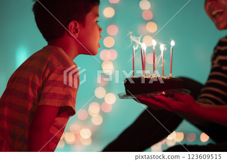 Boy blowing out candles on birthday cake held by parent Boy blowing out candles on birthday cake held by parent 123609515