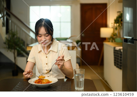 Happy young woman sitting at dining table enjoying a delicious plate of spaghetti 123610459