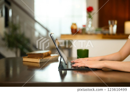 Close up of woman hands typing on digital tablet with a keyboard case on dinning table Close up of woman hands typing on digital tablet with a keyboard case on dinning table 123610499