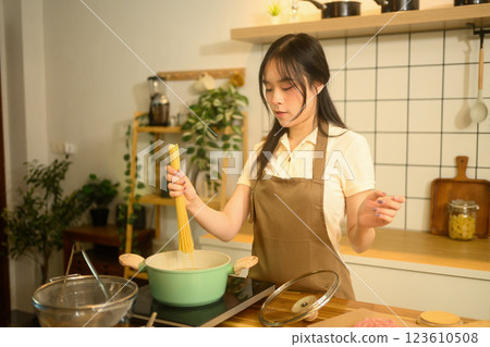 Beautiful woman dropping spaghetti into a pot of boiling water while cooking in a stylish home kitchen 123610508