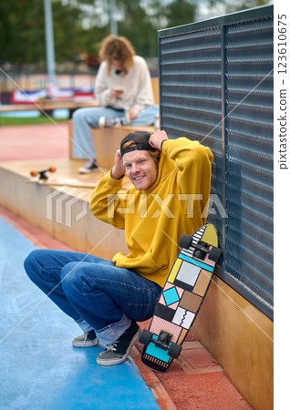 Tall guy in yellow hoodie standing with skateboard in hands 123610675