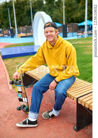Positive smiling guy in yellow hoodie sitting on the bench 123610682