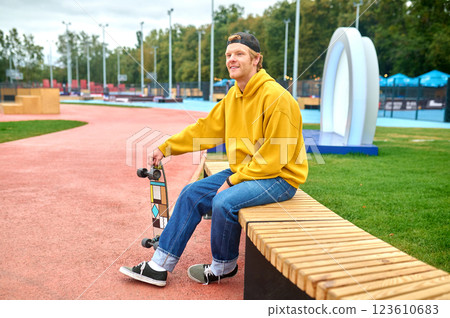 Positive smiling guy in yellow hoodie sitting on the bench 123610683