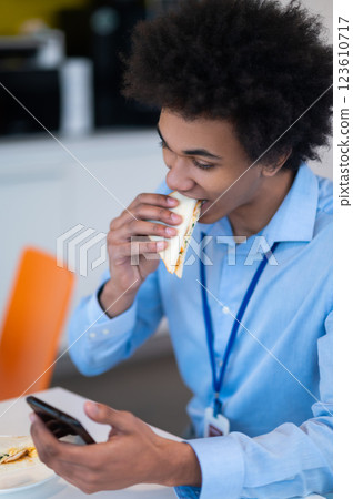 Hungry busy man having snack and scrolling online on smartphone Hungry busy man having snack and scrolling online on smartphone 123610717