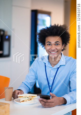 Man feeling hungry enjoying snack while browsing internet on his smartphone in office kitchen Man feeling hungry enjoying snack while browsing internet on his smartphone in office kitchen 123610718