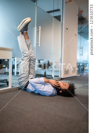 Relaxed man lying on floor with raised legs and talking on mobile phone in office 123610733