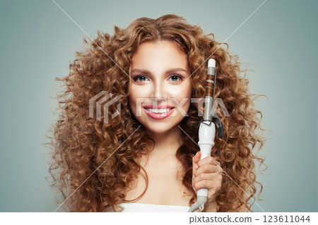 Glamorous brunette model using curling iron on grey background. Coiffure, beauty salon  123611044
