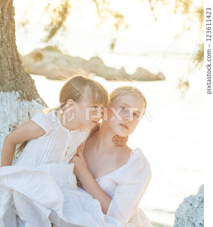 Portrait of two sisters, kid and teenage girl sitting on the tree against background of sea 123611423
