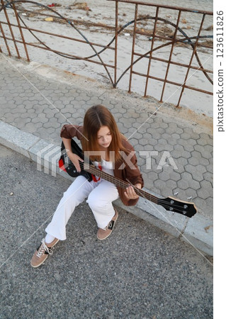 Girl Plays The Bass Instrument Sitting On The Step Near The Street At Evening 123611826