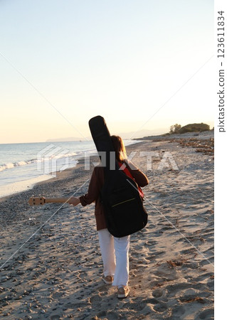 Girl Walks And Plays The Bass Instrument On The Beach Near The Ocean At Sunset 123611834