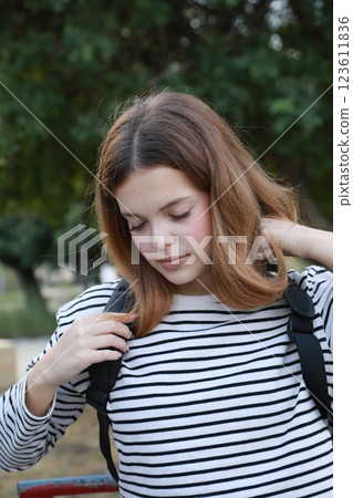 Girl Puts Backpack With Ukulele Musical Instrument On Shoulders And Walks In A Park Girl Puts Backpack With Ukulele Musical Instrument On Shoulders And Walks In A Park 123611836