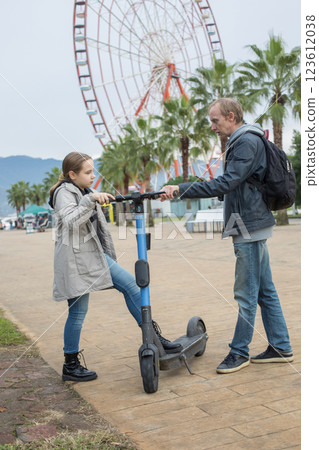 Cute child girl and her father with electric scooter sharing on city street. Happy holiday, vacation Cute child girl and her father with electric scooter sharing on city street. Happy holiday, vacation 123612038