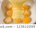 Cooking pouring cake batter over peeled mandarin oranges in baking dish. 123612099