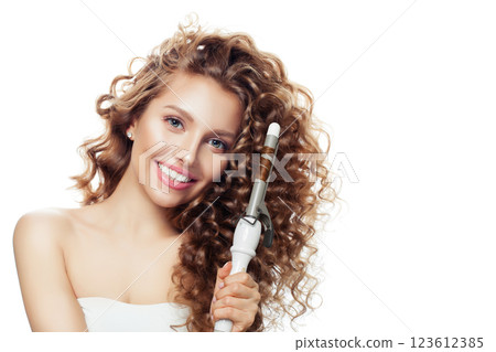 Cheerful woman with curly hairstyle using hot curling tongs iron, indoor fashion portrait. 123612385