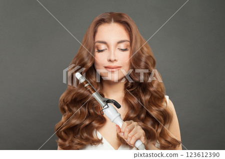 Lovely woman with curly hairstyle using hot curling tongs iron, indoor fashion portrait 123612390