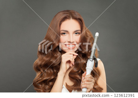 Nice brunette model using curling iron on grey background. 123612391