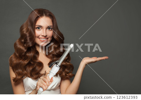 Healthy brown haired woman with shiny long curly hairstyle showing curling iron. Healthy brown haired woman with shiny long curly hairstyle showing curling iron. 123612393