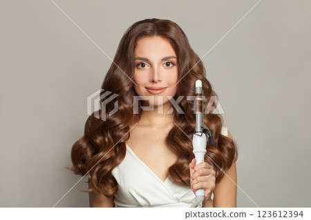Lovely brunette model using curling iron on white background. Lovely brunette model using curling iron on white background. 123612394