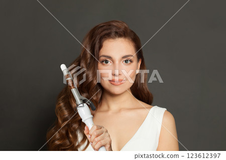 Gorgeous brown haired woman with shiny long curly hairstyle showing curling iron. Gorgeous brown haired woman with shiny long curly hairstyle showing curling iron. 123612397
