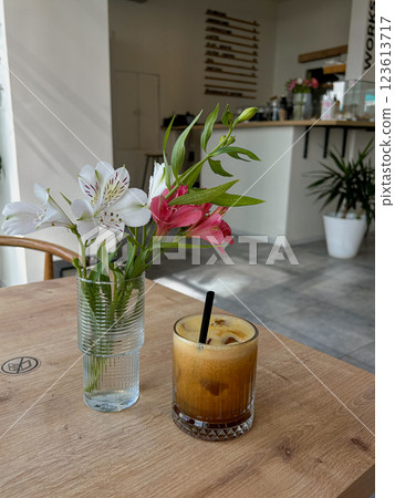 A wooden cafe table with a glass of iced coffee and a vase of fresh flowers. Suitable for coffee branding, caf marketing, lifestyle blogs, and interior photography A wooden cafe table with a glass of iced coffee and a vase of fresh flowers. Suitable for coffee branding, caf marketing, lifestyle blogs, and interior photography 123613717