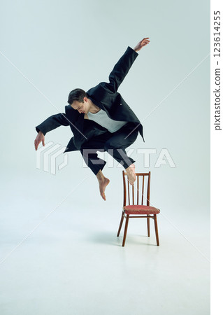 Elegant man leaping off vintage chair in raw expression of freedom and corporate rebellion against white studio backdrop. 123614255