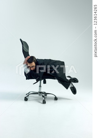 Man dressed formal attire, dynamically stretched and defying business norms lying on office chair against white studio background. Man dressed formal attire, dynamically stretched and defying business norms lying on office chair against white studio background. 123614265