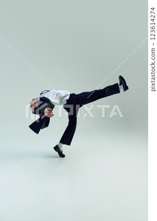 Young businessman balancing in dynamic pose with extended arms and arched body against white studio background. 123614274