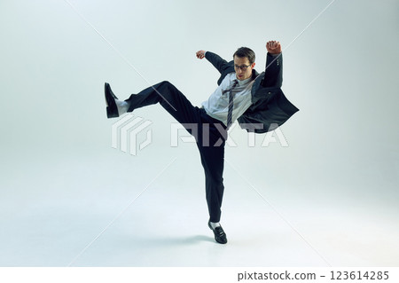 Businessman mid-air, one leg lifted, arms open, striking confident pose against white studio background. Concept of business, risk-taking Businessman mid-air, one leg lifted, arms open, striking confident pose against white studio background. Concept of business, risk-taking 123614285
