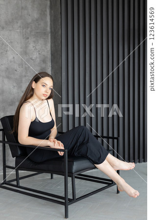 Young woman relaxing on a modern black armchair in a minimalist interior Young woman relaxing on a modern black armchair in a minimalist interior 123614569