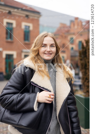 Stylish attractive young smiling 30s woman walking on city street in winter outfit, old town. Urban lifestyle concept. Portrait of happy woman looking at camera outdoor. High quality photo. 123614720