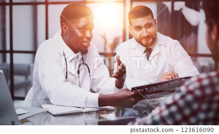 Male doctors and a patient at the reception are discussing an x-ray of the brain. 123616090