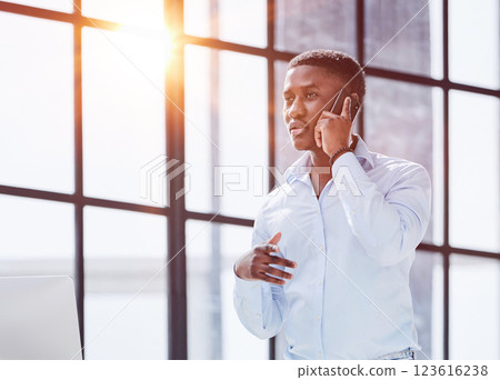 young man in a blue shirt talking on the phone while standing in his office 123616238