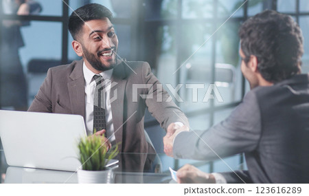 two confident business men shaking hands at the office table two confident business men shaking hands at the office table 123616289