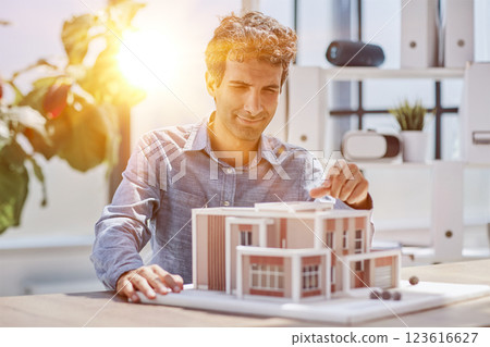 young caucasian engineer man making building model with the use of drawings and notes in office. smart designer assembles a complex structure 123616627