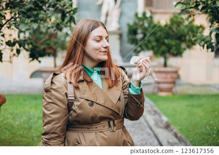 Happy 30s woman holding Sicilian cannolo tube pastry filled with cream outdoors. Travel, Italy, food and holidays concept. Young woman eating traditional delicious cake cannoli, Traveling Europe 123617356